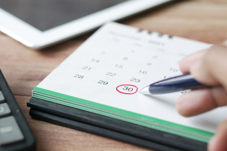 Hand marking a date on a paper calendar, representing scheduled recovery check-ins and planned support.