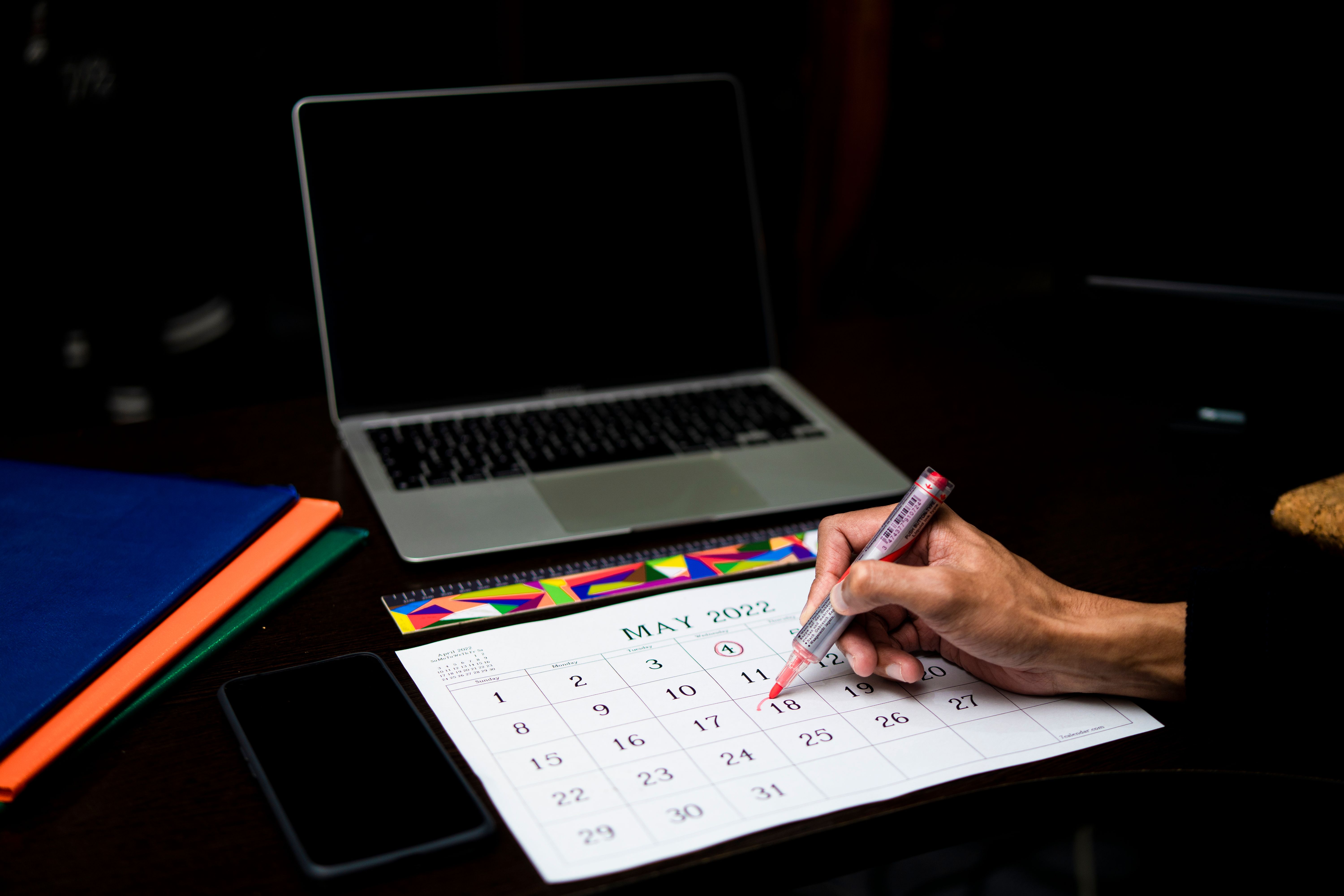 Person planning on a calendar beside a laptop and phone, illustrating reminders for recovery check-ins.